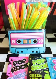 an old school cassette with some colored straws in front of it on a black and white checkered table