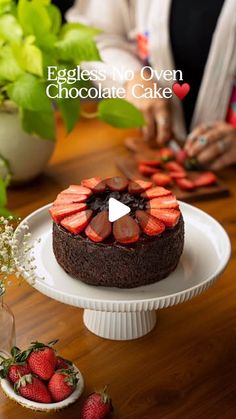 a chocolate cake topped with sliced strawberries on top of a white plate next to flowers