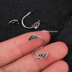 a pair of silver earrings with bats on the back of them, sitting in someone's hand