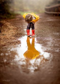 a little boy standing in the middle of a puddle wearing red boots and holding an umbrella