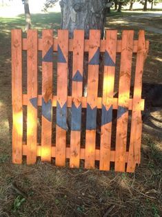 a wooden fence with an arrow painted on it in front of a tree and grass