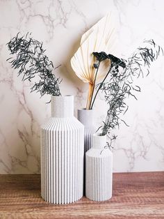 two white vases sitting on top of a wooden table next to a flower arrangement