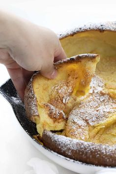 a person scooping some food out of a pie pan with powdered sugar on top