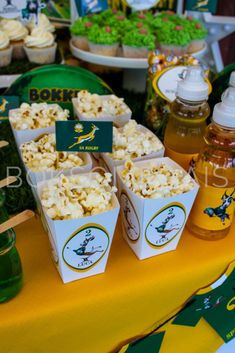 a table topped with lots of food covered in green and yellow paper cups filled with popcorn