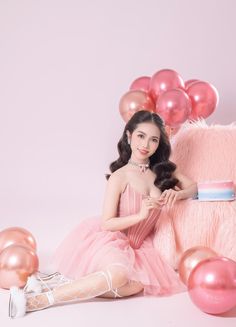 a woman in a pink dress sitting next to a teddy bear with balloons around her