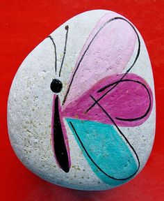 a painted rock sitting on top of a red table next to a white and blue butterfly