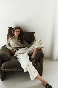 a woman sitting on top of a green chair next to a white wall and wearing black shoes