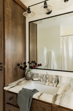 a bathroom vanity with marble counter top and wooden cabinetry, along with a large mirror over the sink