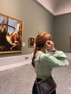 a woman taking a photo of paintings in an art museum with her cell phone to her ear