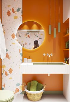 a bathroom with an orange wall and white counter top, mirror above the sink, and green chair in front of it