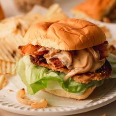 a chicken sandwich with lettuce and tomato sauce on a plate next to chips