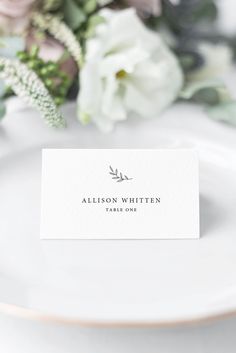 a place card sitting on top of a white plate next to some flowers and greenery