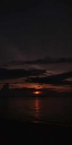 the sun is setting over the ocean with dark clouds