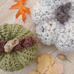 two crocheted pumpkins sitting on top of a wooden table next to leaves