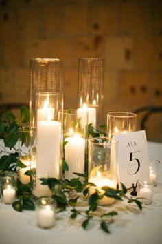 candles and greenery are arranged in glass vases on a wooden table with blue flowers