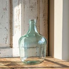 a green glass bottle sitting on top of a wooden table next to a white door