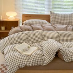 an unmade bed with checkered sheets, pillows and a book on the end