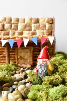 a gnome figurine sitting in front of a house made out of rocks and grass