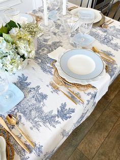 a table set with blue and white plates, silverware and flowers in vases