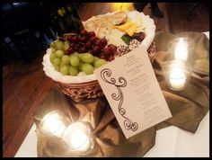 a table topped with a basket filled with grapes and cheese next to two lit candles