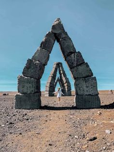 a person standing in front of an arch made out of rocks on top of a dirt field