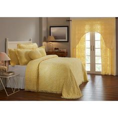 a bed with yellow comforter and pillows in a room next to a window,