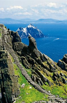 stairs lead down to the top of a rocky cliff by the ocean with snow capped mountains in the background