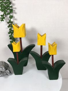 three yellow paper flowers sitting on top of a white table next to a green plant