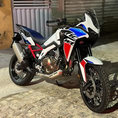 a red, white and blue motorcycle parked in front of a garage