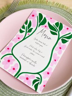 a pink and green plate with a menu card on it, along with silverware