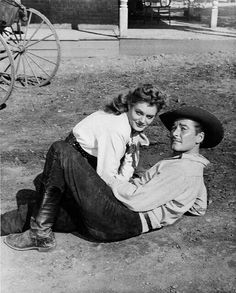 an old photo of a man sitting on the ground next to a woman wearing a cowboy hat