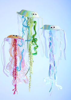 three plastic jelly fish hanging from strings on a white wall with blue and green background