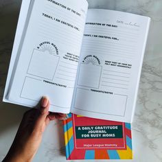 a hand holding an open book on top of a white table with writing in it