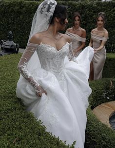 two women in wedding gowns are walking through the grass with one woman wearing a veil