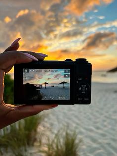 a person holding up a camera to take a photo on the beach with sunset in the background