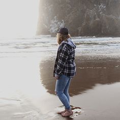 a woman standing on top of a sandy beach next to the ocean in front of a cliff