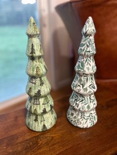 two ceramic christmas trees sitting on top of a wooden table