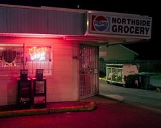 a neon sign is lit up in front of a grocery store with the door open