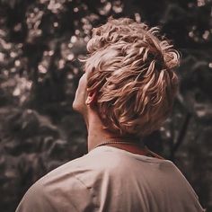 a person standing in front of trees with their head turned to the side looking up