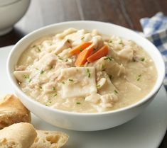 a bowl of chicken and dumpling soup on a plate next to some bread rolls