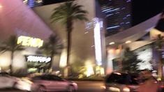 cars are driving down the street in front of a building at night with palm trees