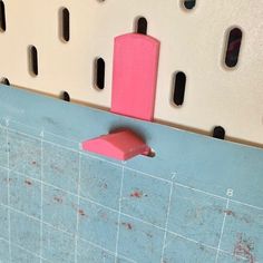 a pink object sticking out of the side of a blue tiled wall with holes in it