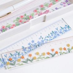 two rulers with flowers on them next to a pen and ruler, which are both decorated in different colors