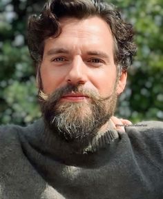 a man with a beard and moustache looks at the camera while wearing a sweater