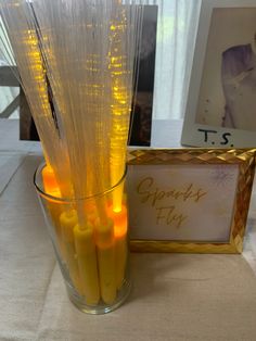 a vase filled with yellow candles on top of a table next to a framed photo