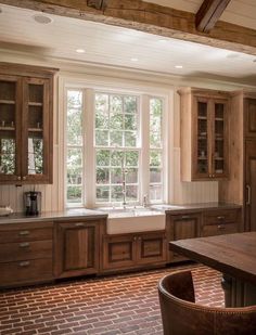 a kitchen with brick flooring and wooden cabinets in the center, along with a large window