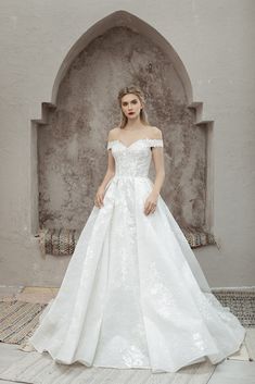 a woman in a white wedding dress standing on a rug with an archway behind her