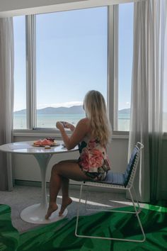 a woman sitting at a table in front of a window looking out onto the ocean