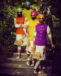 three men dressed in brightly colored clothing standing on steps with trees and bushes behind them