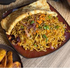 a plate with noodles and vegetables on it next to some fried plantain wedges